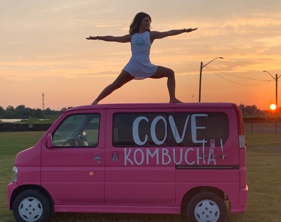 A woman is doing yoga on top of a pink van.